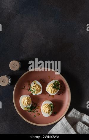 Healthy deviled eggs topped with fresh herbs on pink plate, flatbread crackers, perfect Easter party appetizer, high angle view, copy space Stock Photo
