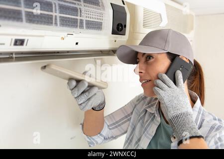 female technician repairing air conditioner and talking on telephone Stock Photo