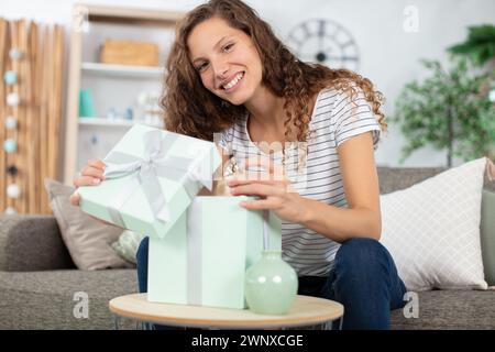 happy woman sitting on couch at home opening carton box Stock Photo