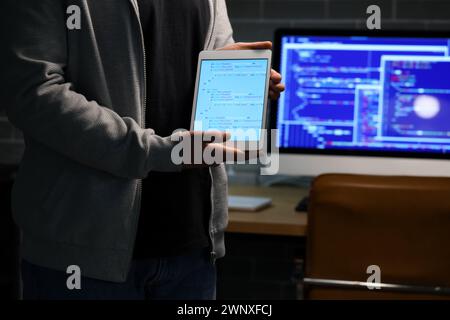 Hacker with tablet computer in dark room, closeup Stock Photo