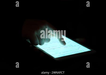 Hacker using tablet computer in dark room, closeup Stock Photo