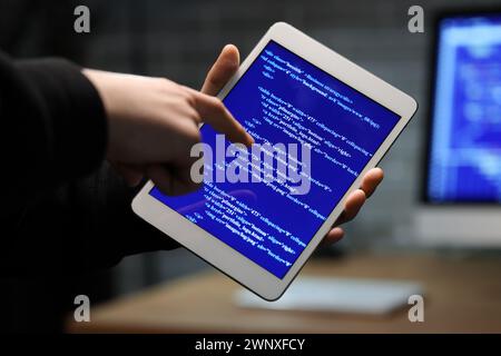 Hacker using tablet computer in dark room, closeup Stock Photo