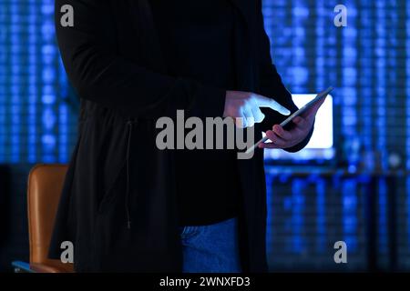 Hacker using tablet computer in dark room, closeup Stock Photo