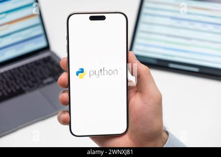 PRAGUE, CZECH REPUBLIC - JANUARY 21 2024: Python logo on the screen of smartphone in mans hand on the workplace background.  Stock Photo