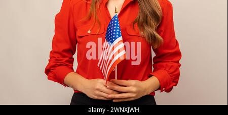 Faceless shot of a young woman wearing red shirt holding USA flag with both hands. Stock Photo