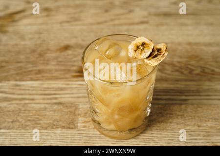 A cocktail with a slice of dried banana and ice on a wooden table Stock Photo