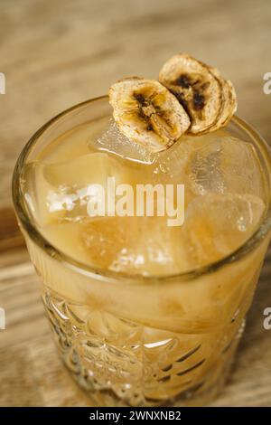 A cocktail with a slice of dried banana and ice on a wooden table Stock Photo