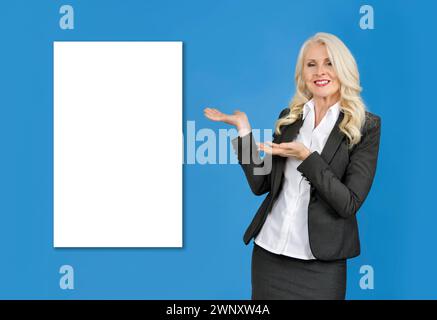 Attractive business woman against blue background with hands pointing towards blank white space behind her. Fill in the blank Stock Photo