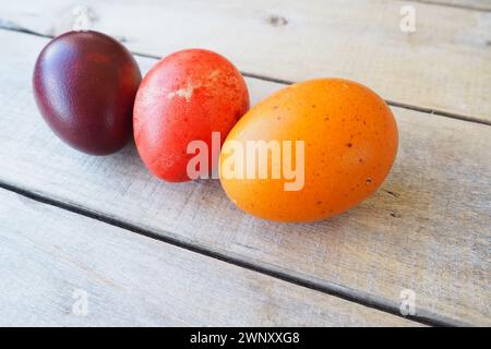 Easter colorful eggs close-up on wooden table, paschal background. Three boiled chicken eggs with red, orange and brown shells, dyed with onion peel. Stock Photo