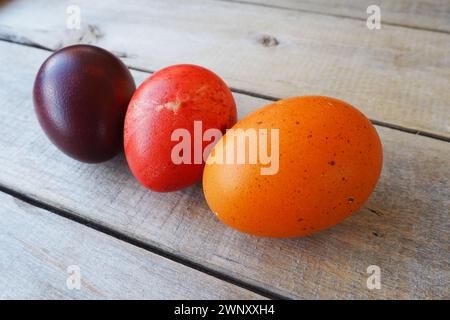 Easter colorful eggs close-up on wooden table, paschal background. Three boiled chicken eggs with red, orange and brown shells, dyed with onion peel. Stock Photo