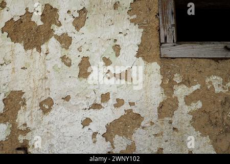 The wall of a residential old house built with bricks made from mud, cow dung and straw. Peeling plaster. Serbia, ancient building technology. Texture Stock Photo