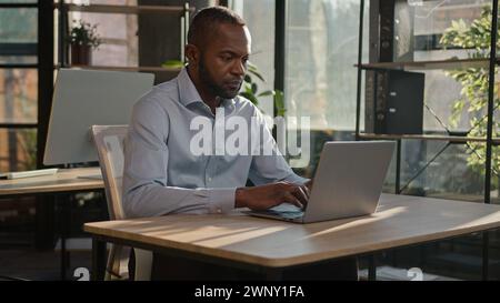 Focused on computer work adult businessman African American senior 40s man worker employer manager specialist programmer typing on laptop at office Stock Photo