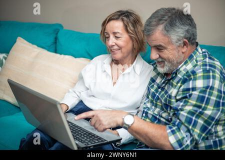 Elderly retired couple pointing at computer screen while discovering new technologies from the sofa at home Stock Photo