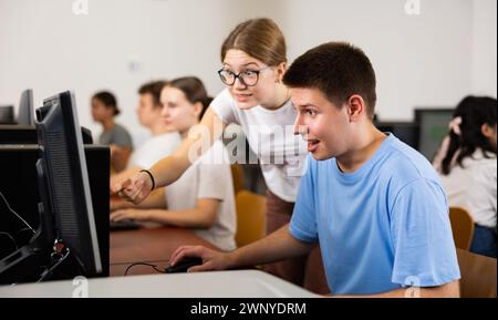 Positive classmates smiling and looking at screen of PC while learning computer science in the classroom Stock Photo