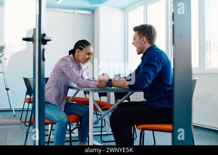 In a modern startup office, a businessman and a businesswoman business colleagues engage in a symbolic arm-wrestling match, reflecting teamwork Stock Photo