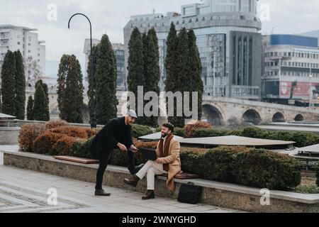 Two businessmen engage in a serious discussion over a laptop while sitting outside. They are focused, exchanging ideas, and working collaboratively. Stock Photo