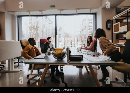 A multicultural team collaborates in a well-lit office environment, focused on work discussion. The modern interior and teamwork are front and center. Stock Photo