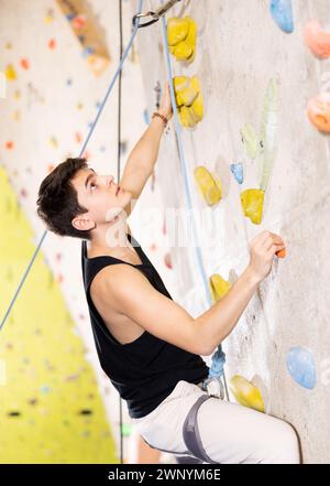 Determined young man doing his best at climbing artificial wall Stock Photo
