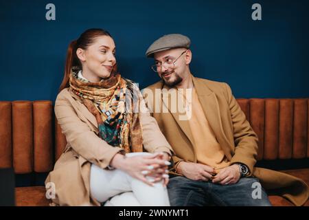 Handsome, male employee flirting with his female colleague at work while sitting on a sofa during the break. Stock Photo