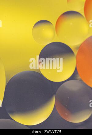 Oil droplets in water reflecting yellow, grey , and orange background Stock Photo
