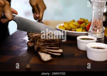 Hands cut grilled meat medium well or rib eye steak on wooden cutting board with grilled potato. close up. Stock Photo