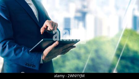 Businessman in suit holding digital tablet while standing near the window in modern office.Abstract light background with copy space. Stock Photo