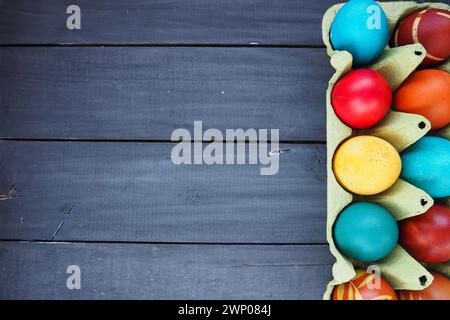 Multi-colored eggs painted with gouache and onion peel in a cardboard box on a wooden table background. Ten boiled eggs. Postcard poster for Easter Stock Photo