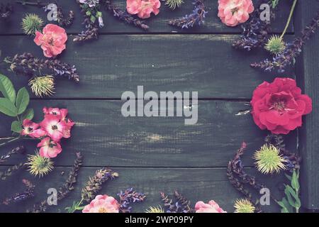 Flowers in a circle on a wooden background. Postcard for the holiday. Roses, geraniums, lavender, sage and hairy chestnuts are placed along the edges Stock Photo