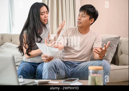 A resentful, angry Asian wife and husband are arguing about family household invoices and high domestic bills, quarreling about the issue of wasting m Stock Photo