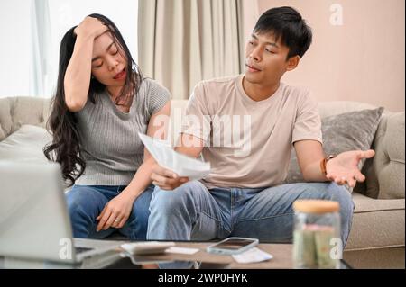 A resentful, angry Asian wife and husband are arguing about family household invoices and high domestic bills, quarreling about the issue of wasting m Stock Photo