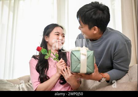 A caring and romantic Asian man is surprising his girlfriend or spouse with a present and flowers at home. romantic couple, happy moment, love, bondin Stock Photo