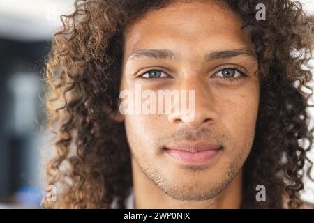 Young biracial man with curly hair and light brown eyes looks directly at the camera Stock Photo