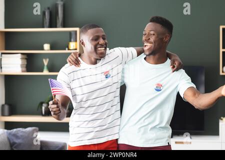 Two young African American men are smiling with I Voted stickers, one holding an American flag Stock Photo