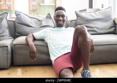 Young African American man with a bright smile sits relaxed on a grey sofa Stock Photo