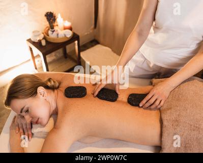 Beautiful woman at spa resort receives hot stone massage. Hot stone massage therapy using smooth, flat, heated stones Stock Photo