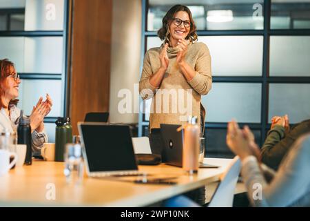 Team of professionals in a modern office, collaborating on a successful project. Businesswomen show leadership and creativity, earning applause and sm Stock Photo