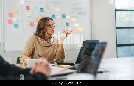 Woman engaging in a collaborative brainstorming session with her colleagues in a boardroom. Business people discuss ideas and manage projects. They wo Stock Photo