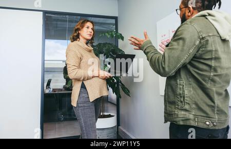 Colleagues in an office brainstorm, discussing business strategy and project planning. Men and women stand together, holding a productive conversation Stock Photo