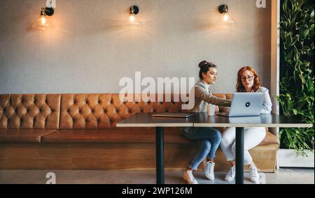 Professionals in a coworking space collaborate and discuss ideas. Businesswomen and coworkers work on laptops, engaging in discussions. They emphasize Stock Photo