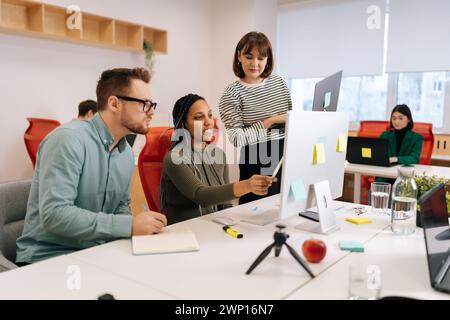 Skilled African female mentor or executive manager boss teaching diverse internes, explaining work pointing at computer screen. Team leader supervisor Stock Photo
