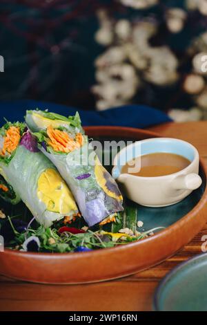 A plate of food with a bowl of sauce next to it. The food is a roll with vegetables and carrots Stock Photo