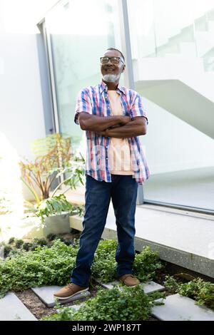 Senior biracial man with glasses stands confidently, arms crossed, wearing a striped shirt and jeans Stock Photo
