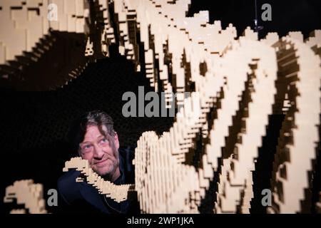 Artist Nathan Sawaya looks at a 6ft long Lego T-Rex, during the preview for the Art of the Brick Lego exhibition at the Boiler House in east London. Picture date: Tuesday March 5, 2024. Stock Photo