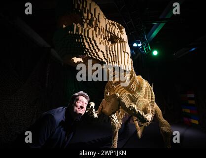 Artist Nathan Sawaya looks at a 6ft long Lego T-Rex, during the preview for the Art of the Brick Lego exhibition at the Boiler House in east London. Picture date: Tuesday March 5, 2024. Stock Photo