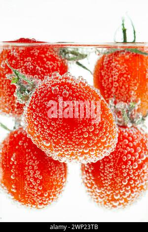 Cherry tomatoes submerged in water with bubbles clinging to the skin Stock Photo