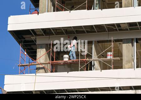 Puerto Vallarta, Jalisco, Mexico - 15 January 2024: Construction worker standing on a platform on a multi storey building plastering a wall Stock Photo