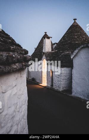 ITALY, PUGLIA, ALBEROBELLO: Street views of the trulli of Alberobello at sunset. The city of Alberobello is famously known as the capital of the trulli, the characteristic stone buildings with a conical roof that never like others, represent in the imagination, the entire Puglia region. It was born as a basic building for agricultural needs, the trulli were in fact used as temporary shelters, deposits, stables, and as the technique was refined, as homes. Stock Photo