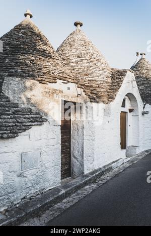 ITALY, PUGLIA, ALBEROBELLO: Street views of the trulli of Alberobello at sunset. The city of Alberobello is famously known as the capital of the trulli, the characteristic stone buildings with a conical roof that never like others, represent in the imagination, the entire Puglia region. It was born as a basic building for agricultural needs, the trulli were in fact used as temporary shelters, deposits, stables, and as the technique was refined, as homes. Stock Photo