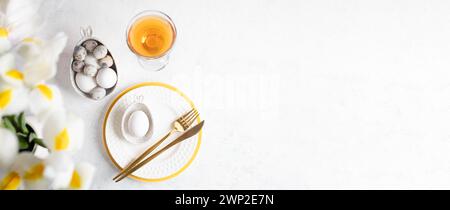 Easter table setting banner. Festive elegant white with yellow restaurant table serving. Figured bowls with eggs, white and yellow plates, golden cutl Stock Photo