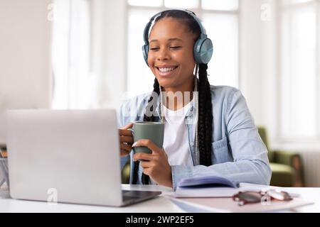 Smiling black female student with headphones studying at laptop Stock Photo